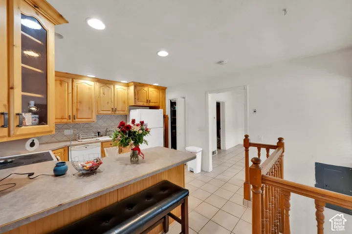 Kitchen featuring natural wood cabinetry, solid surface countertop, tile backsplash, and ceramic tile flooring, complemented by a wooden banister