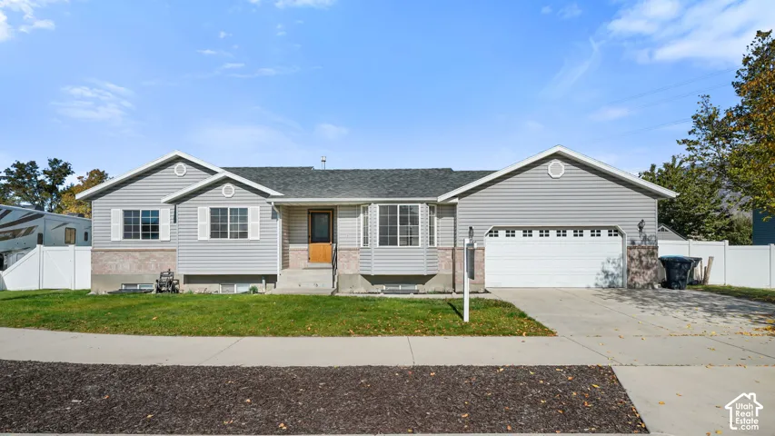 Single-level residence featuring horizontal vinyl siding, brick masonry detailing, a two-car attached garage, a bay window, and a white vinyl perimeter fence
