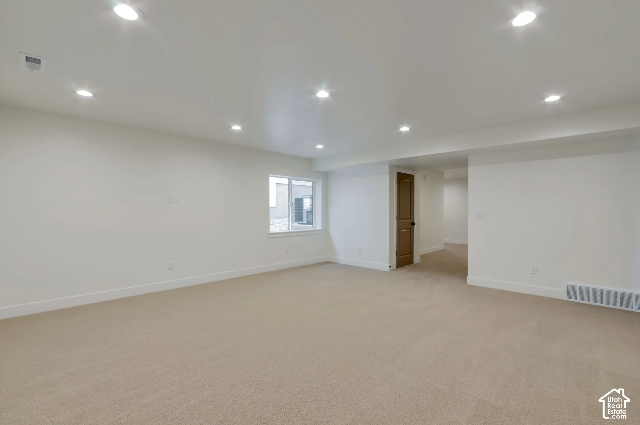 Open-concept room featuring neutral wall-to-wall carpeting, recessed ceiling lighting, and a single-pane window with white trim