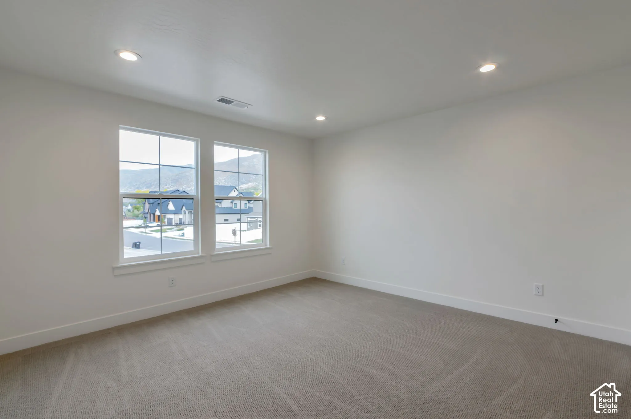 Neutral-toned interior room featuring recessed lighting, dual windows with grid detailing, and wall-to-wall carpeting