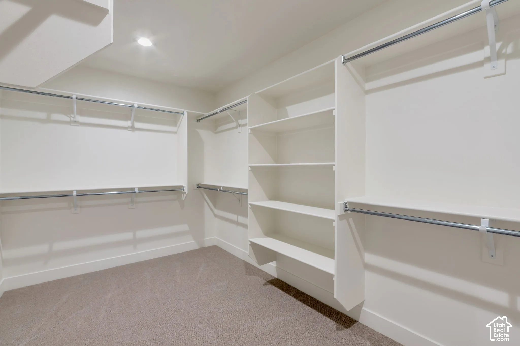 Walk-in closet featuring floor-to-ceiling built-in shelving, multi-level metal hanging rods, and neutral carpeting
