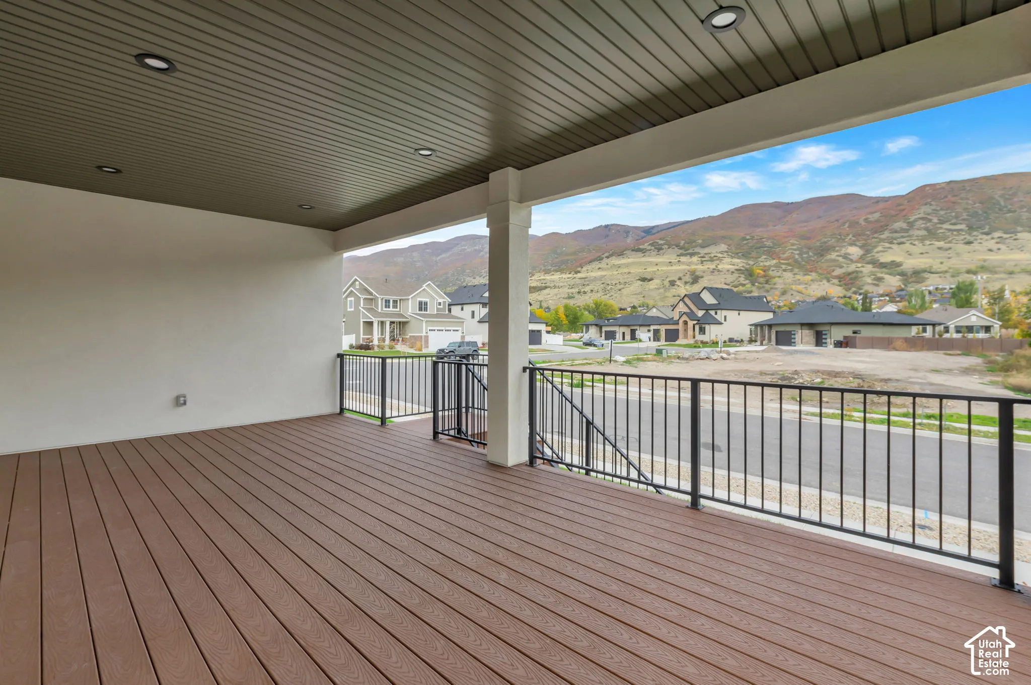 Covered exterior deck featuring composite decking, recessed lighting, a dark-toned beadboard ceiling, and black metal railings, set against a mountain backdrop