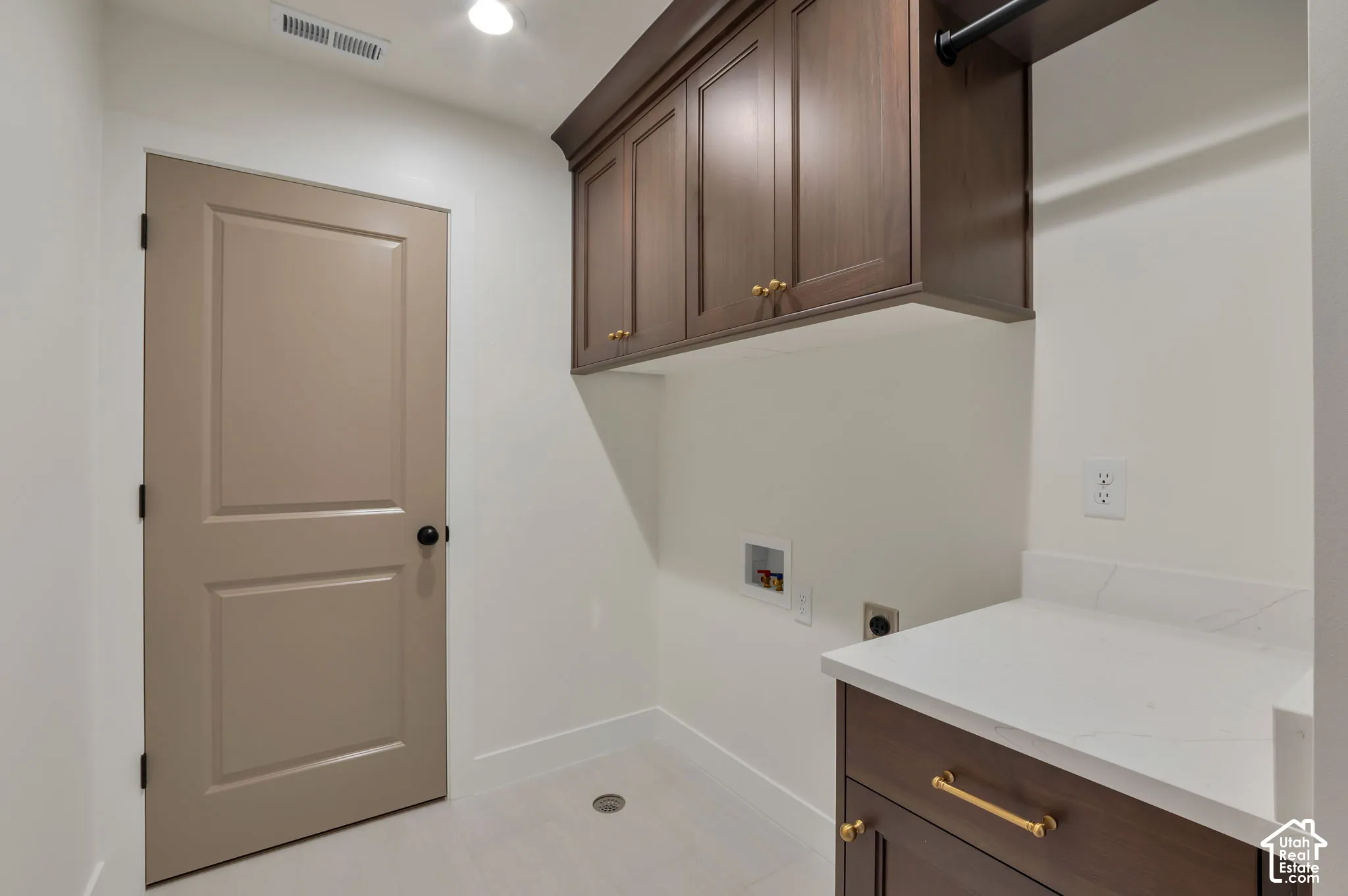 Utility space featuring custom dark wood-finish cabinetry, quartz countertops, brass-finish hardware, and tile flooring