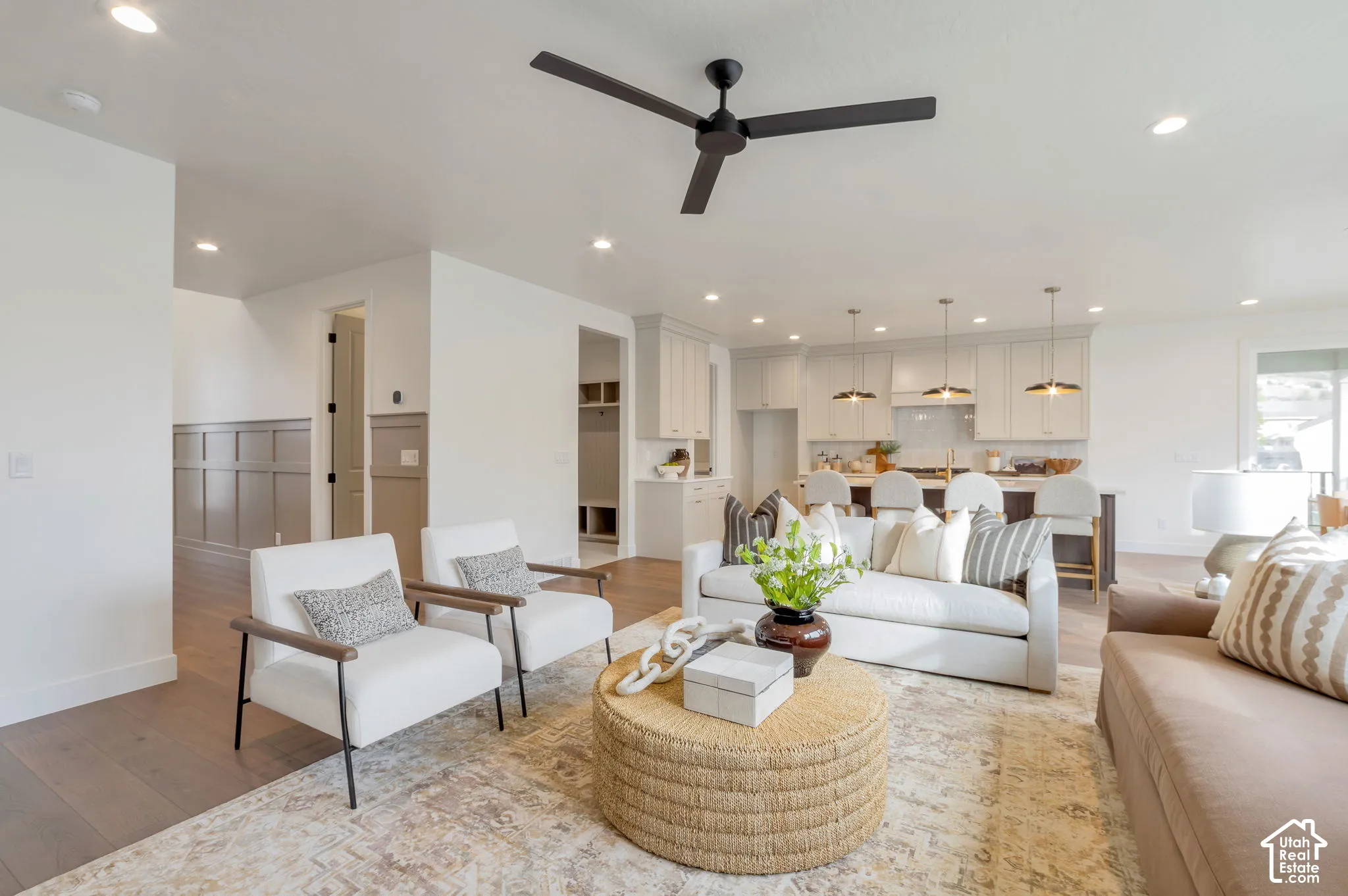 Open-concept living space featuring wood-finish flooring, recessed lighting, a modern ceiling fan, wall wainscoting, and kitchen cabinetry with a central island