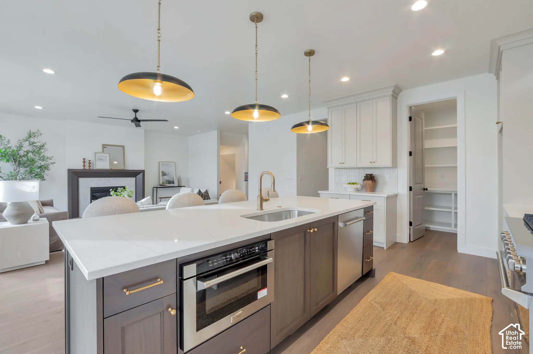 Kitchen island with stone-surface countertop, under-mount stainless steel sink, built-in microwave, three pendant lights, and cabinetry with metal hardware