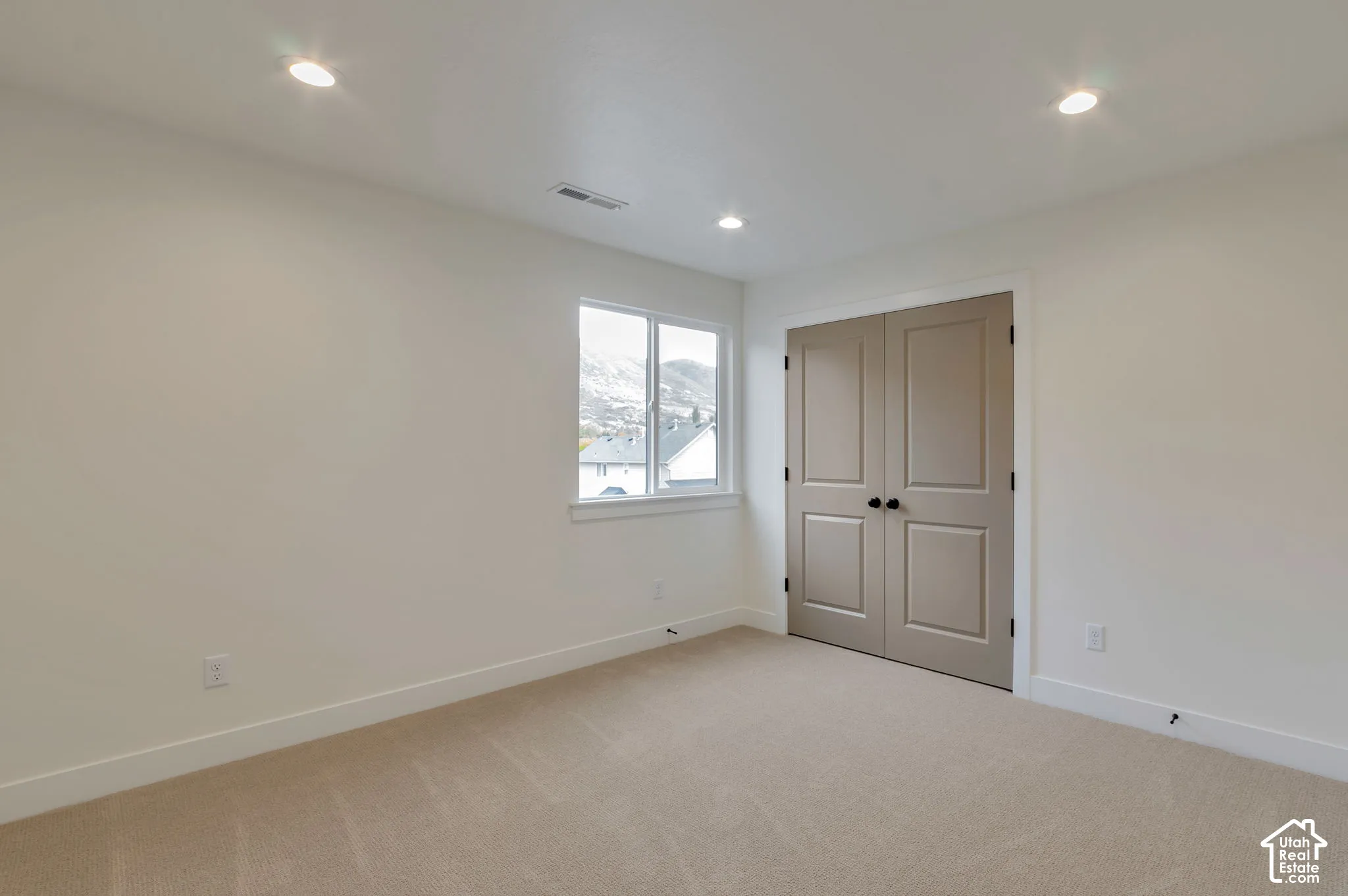 Interior space featuring neutral-toned carpeting, recessed lighting, a single-pane window, and dual-panel closet doors with matte black hardware