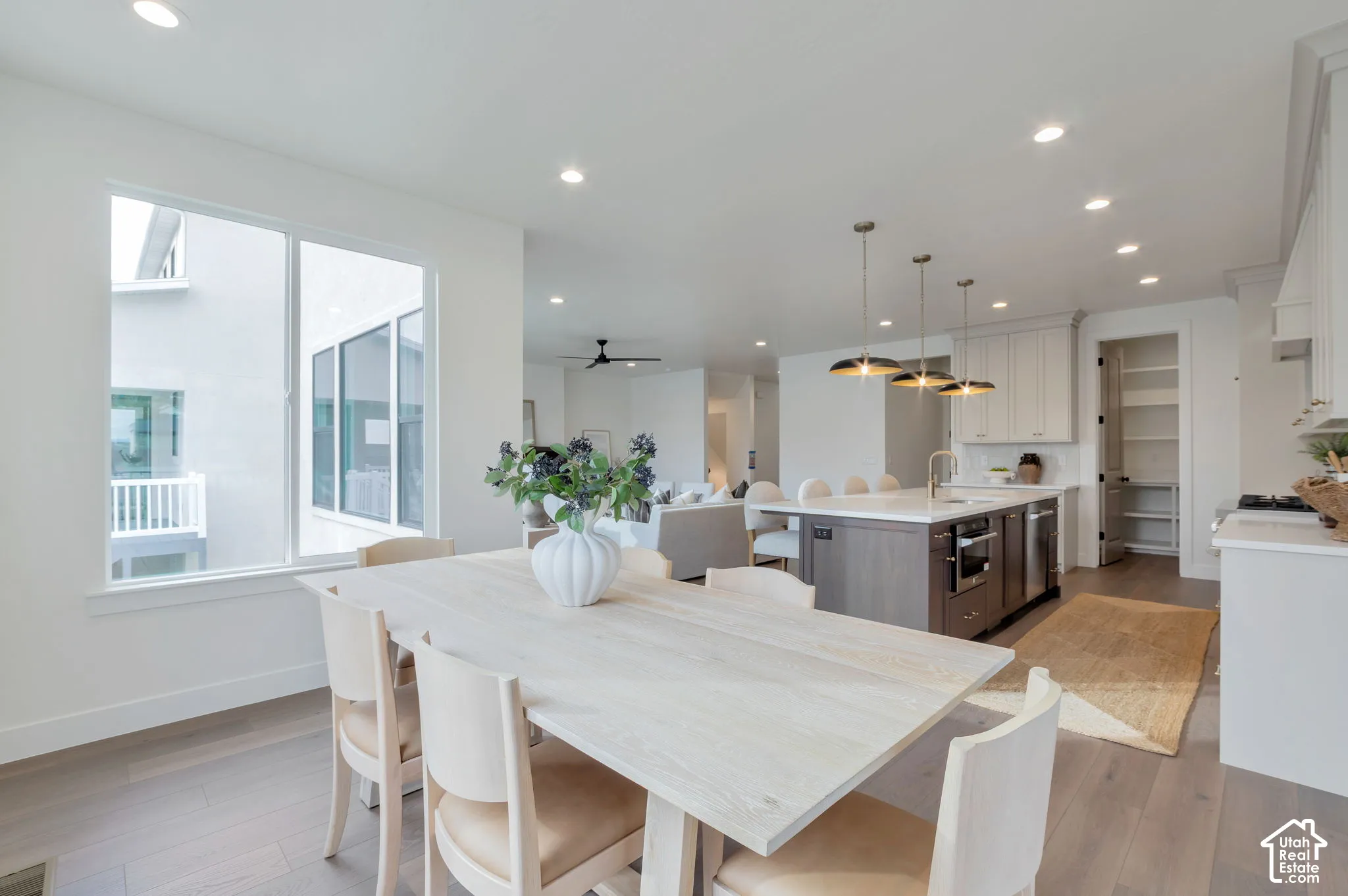 Kitchen featuring a central island with countertop seating, white shaker-style cabinetry, recessed ceiling lighting, three pendant lights, and wood-finish flooring