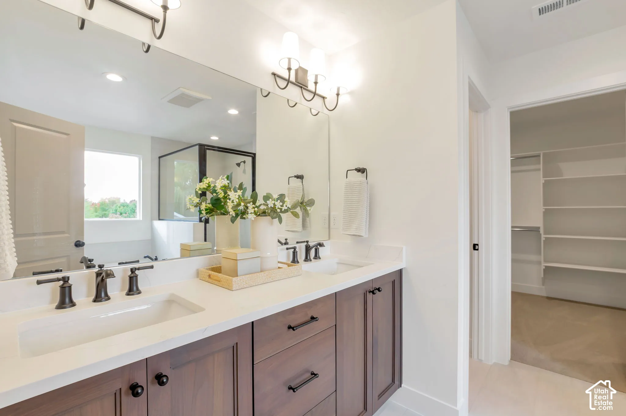 Double vanity featuring wood-finish cabinetry, rectangular undermount sinks, stone countertops, and matte black hardware, paired with a full-width mirror and integrated walk-in closet shelving