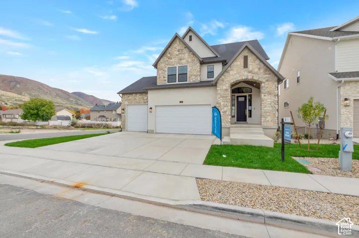 Multi-level exterior featuring stone veneer accents, stucco siding, a three-car garage, and a covered entryway set against a mountain backdrop