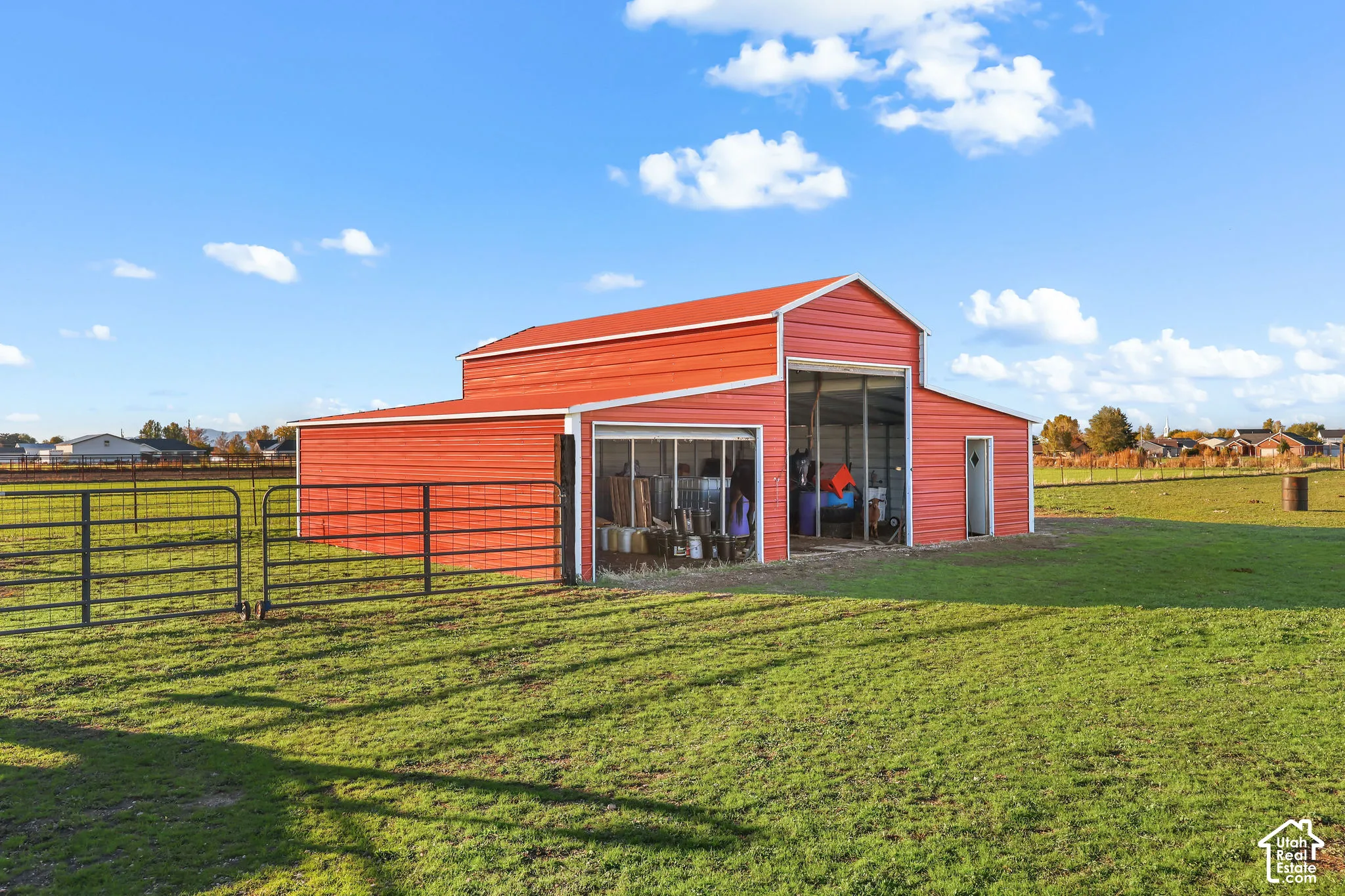 Red metal barn featuring a monitor-style roof, exterior metal cladding, wide sliding access door, single entry door, and perimeter metal fencing on expansive acreage