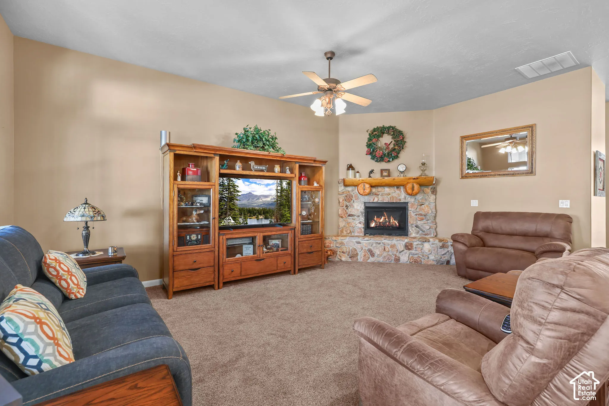 Corner fireplace featuring a stone surround and timber mantel, wooden media cabinetry, and a ceiling fan with integrated lighting