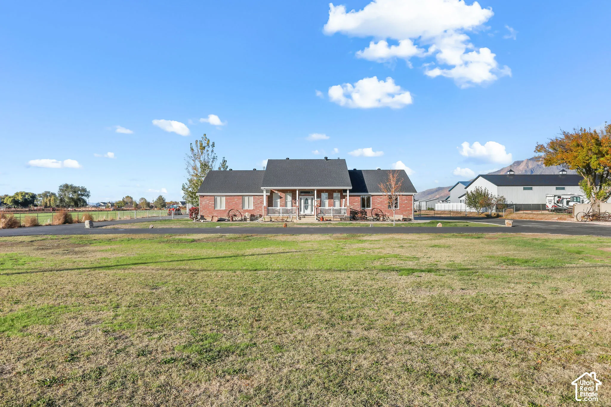 Single-level brick exterior featuring a covered front porch, asphalt shingle roof, paved circular driveway, and expansive grounds