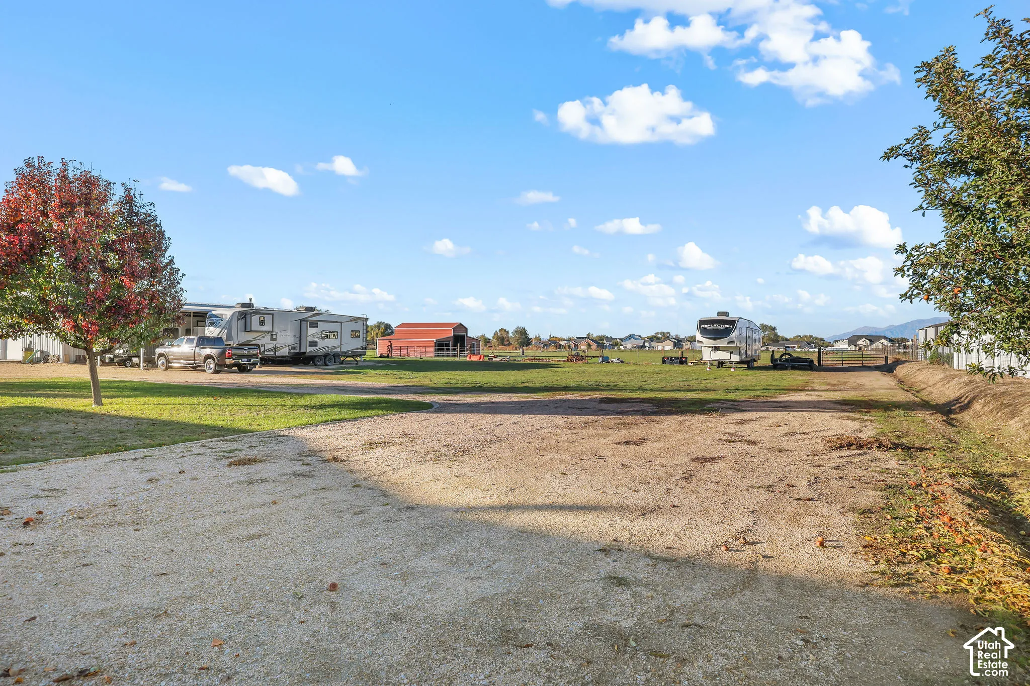 Expansive acreage featuring a gravel driveway, open grass grounds, a red barn structure, and mountain backdrop