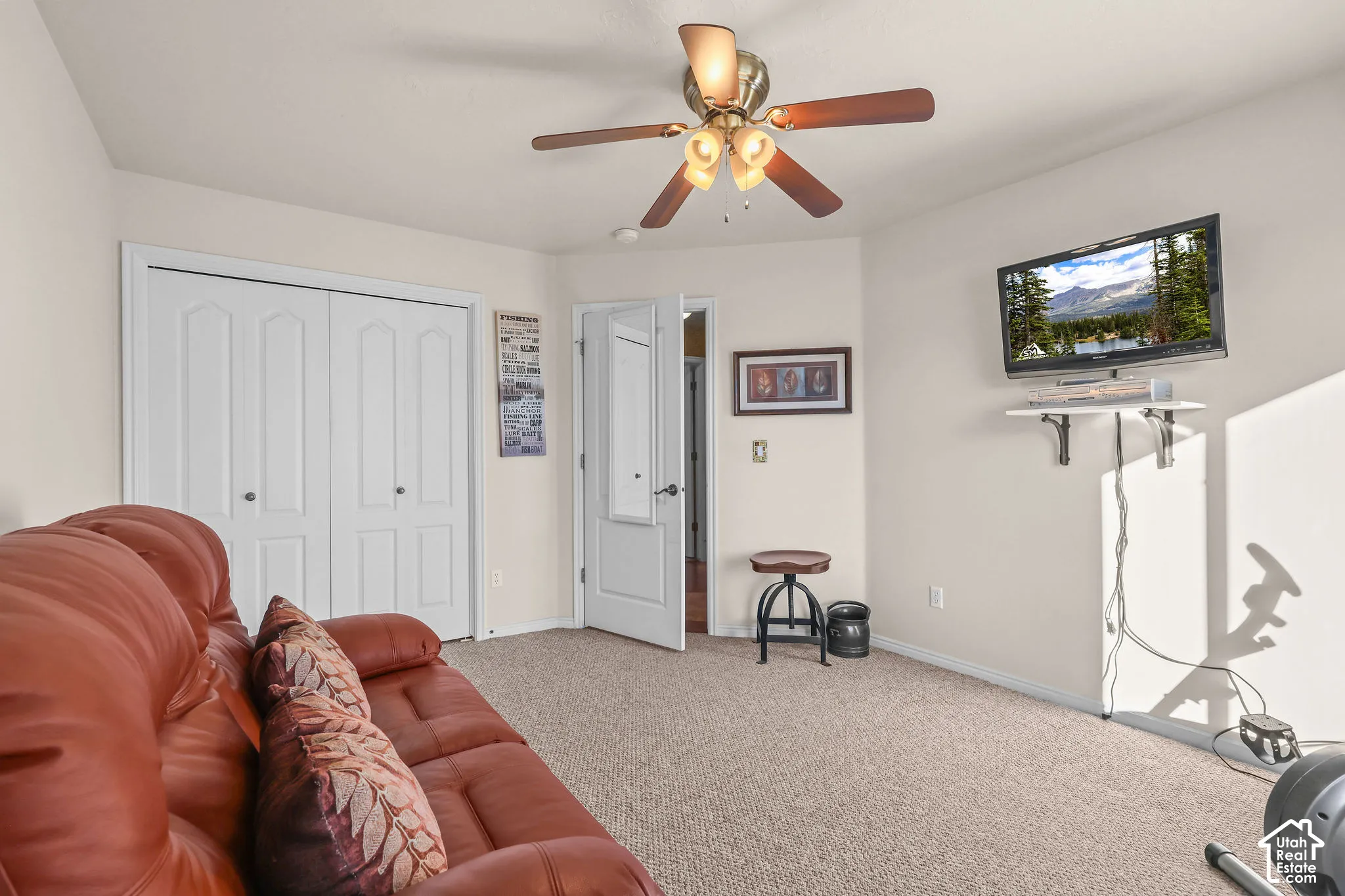 Neutral-toned room featuring a central ceiling fan with multi-light fixture, carpeted flooring, and double-door closet with paneled detailing