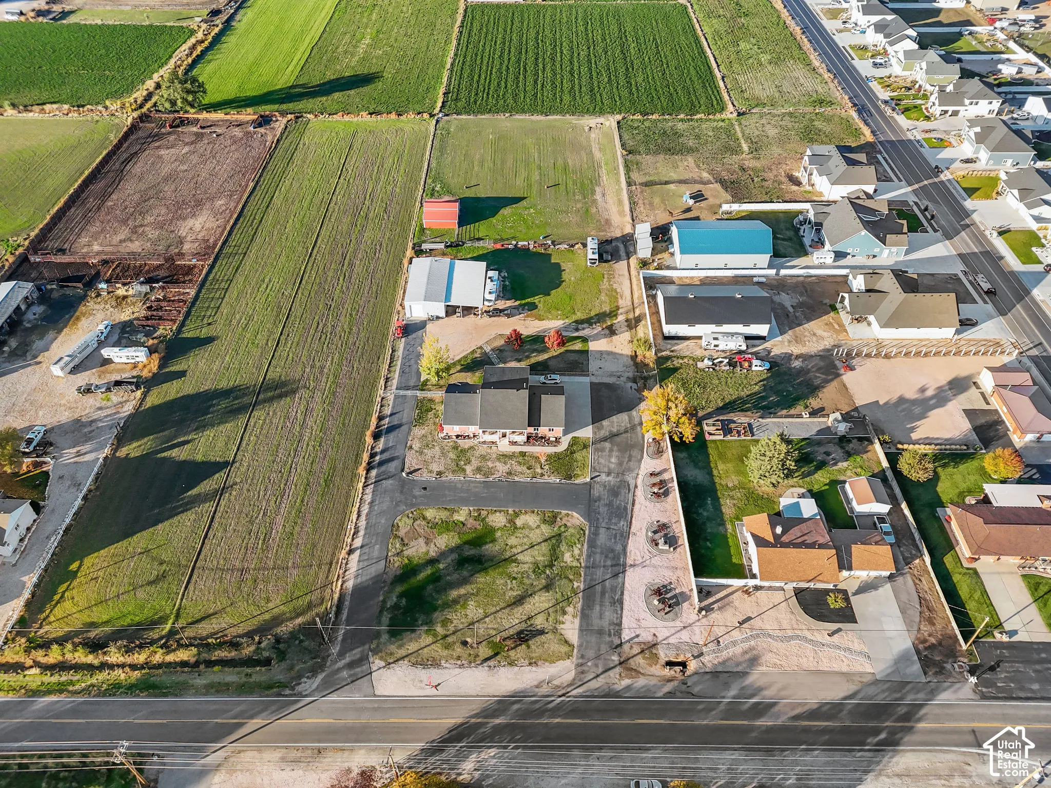 Aerial perspective of an expansive property featuring a paved driveway, a multi-car detached garage, open acreage, and a residence with a dark-shingled roof