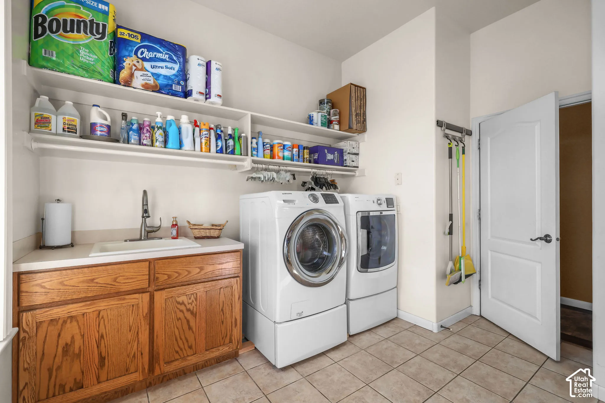 Laundry area featuring tile flooring, wood cabinetry with an integrated sink, gooseneck faucet, and wall-mounted shelving