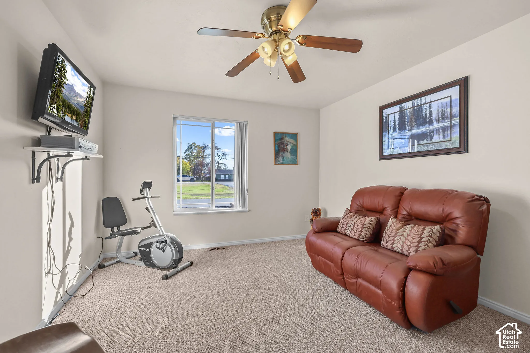 Neutral-toned interior space featuring carpeted flooring, a ceiling fan with integrated lighting, and a single-pane sliding window