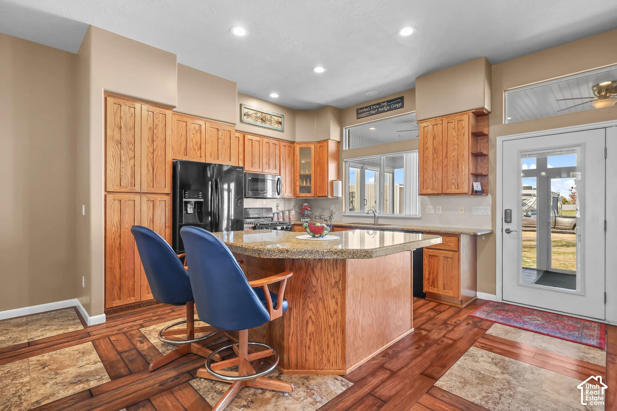 Kitchen featuring wood cabinetry, stone-surfaced countertops, a center island with built-in storage, recessed lighting, and mixed tile and wood-look flooring