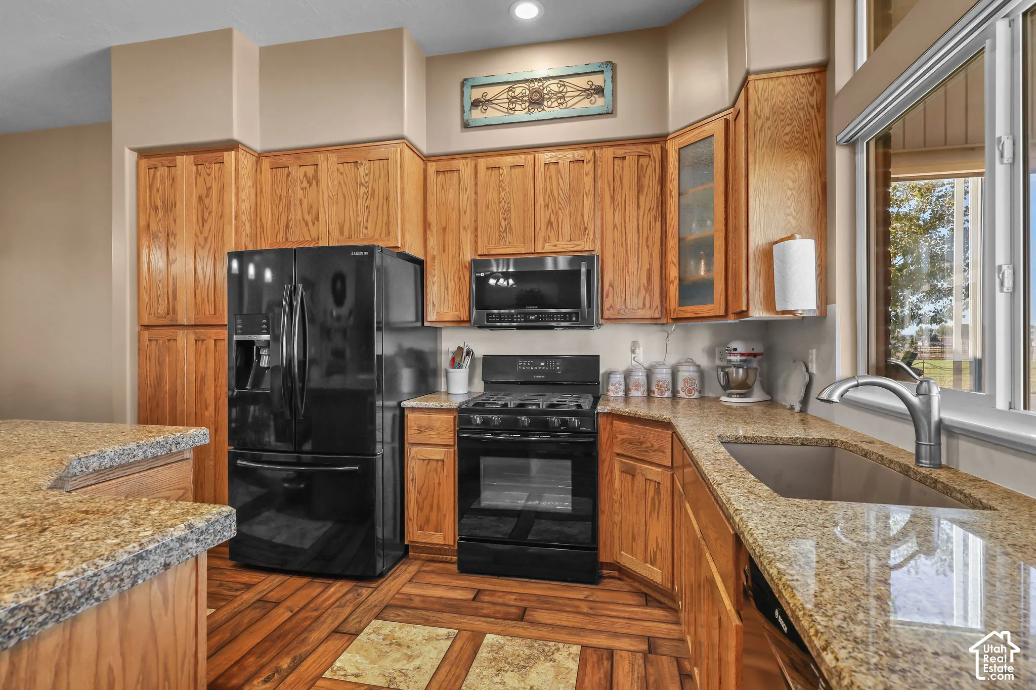 Kitchen featuring wood cabinetry, stone countertops, black appliances, and wood-look flooring