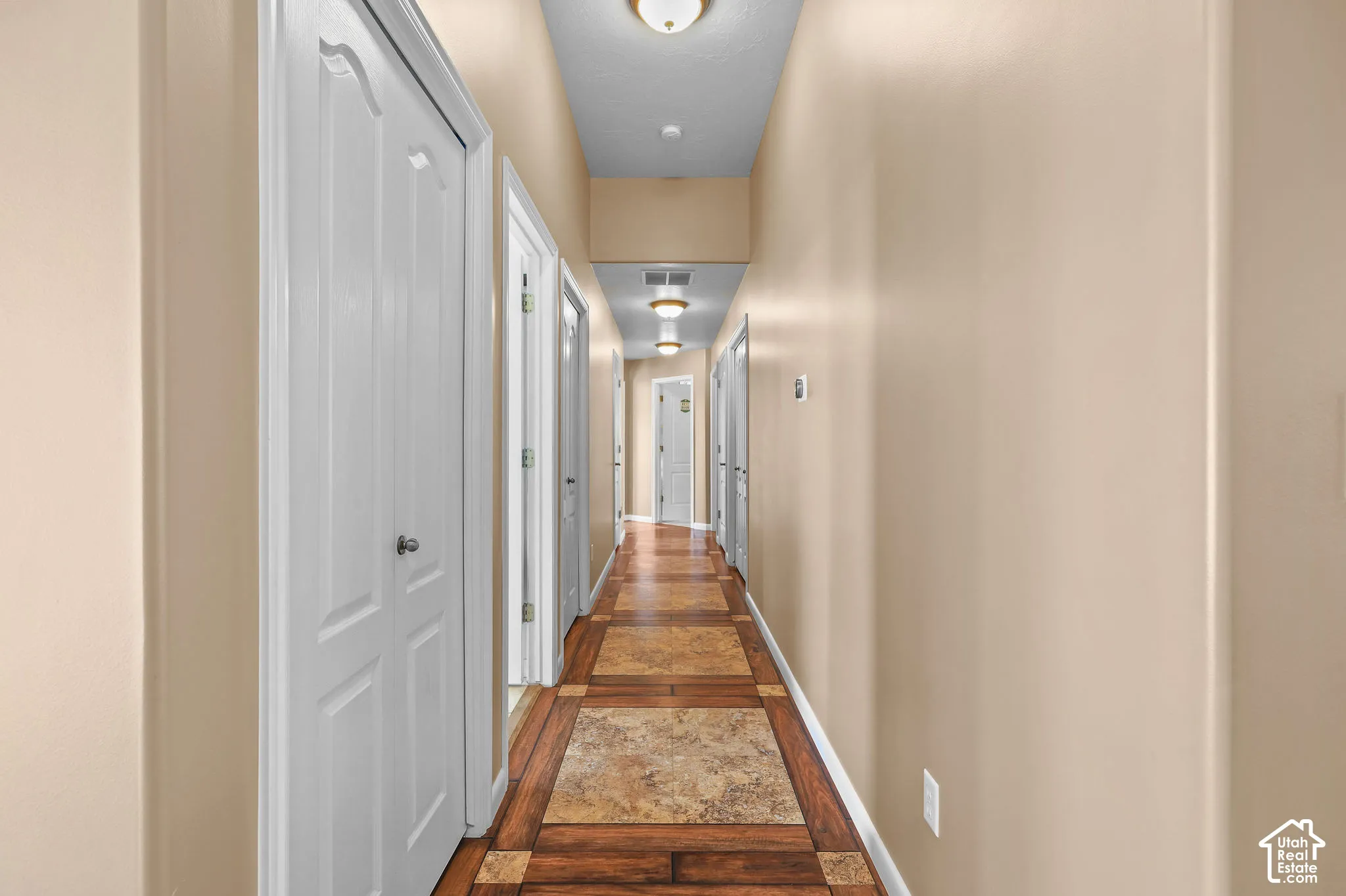 Hallway featuring decorative tile and wood-look flooring, multi-panel doors, and flush-mount ceiling lighting