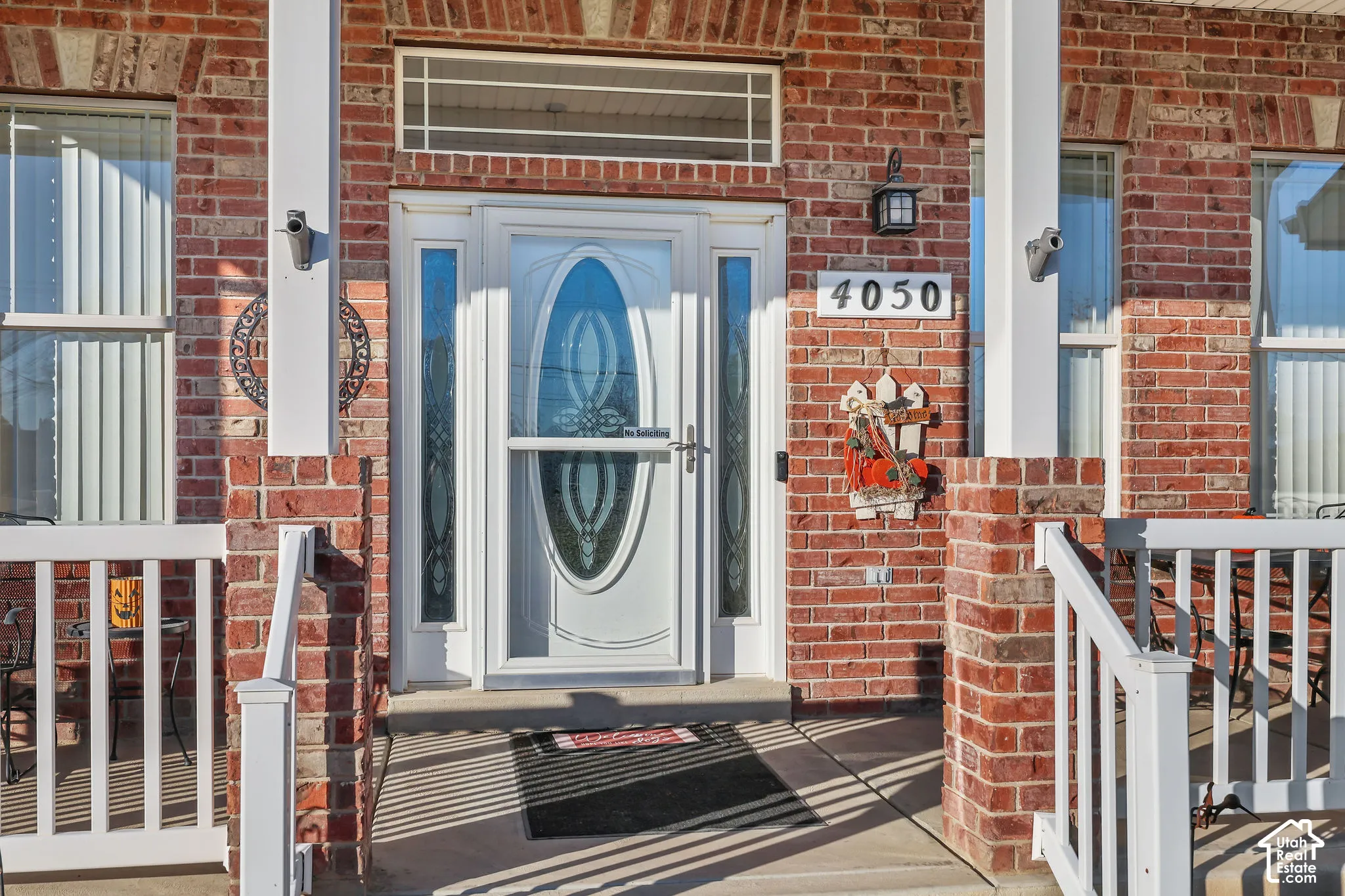 Red brick exterior featuring a covered front porch with white railing, masonry columns, and a central entry door with decorative glass inserts and a transom window