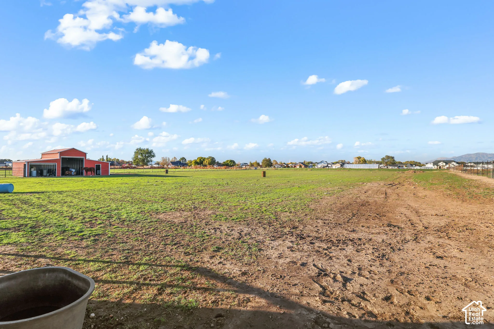 Expansive acreage featuring a red metal-clad barn, wire perimeter fencing, and open pasture land