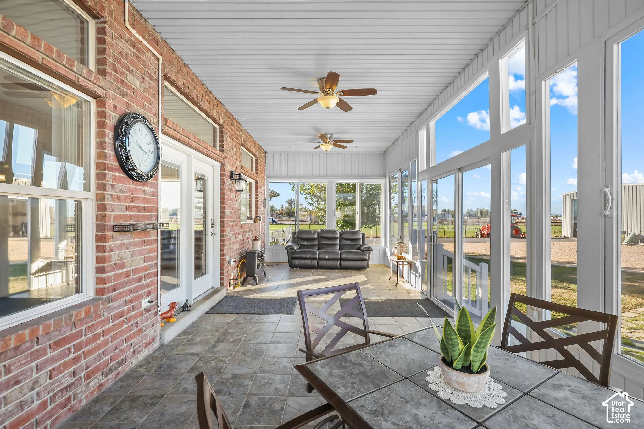 Enclosed sunroom featuring red brick walls, expansive multi-pane windows, neutral tile flooring, and dual ceiling fans