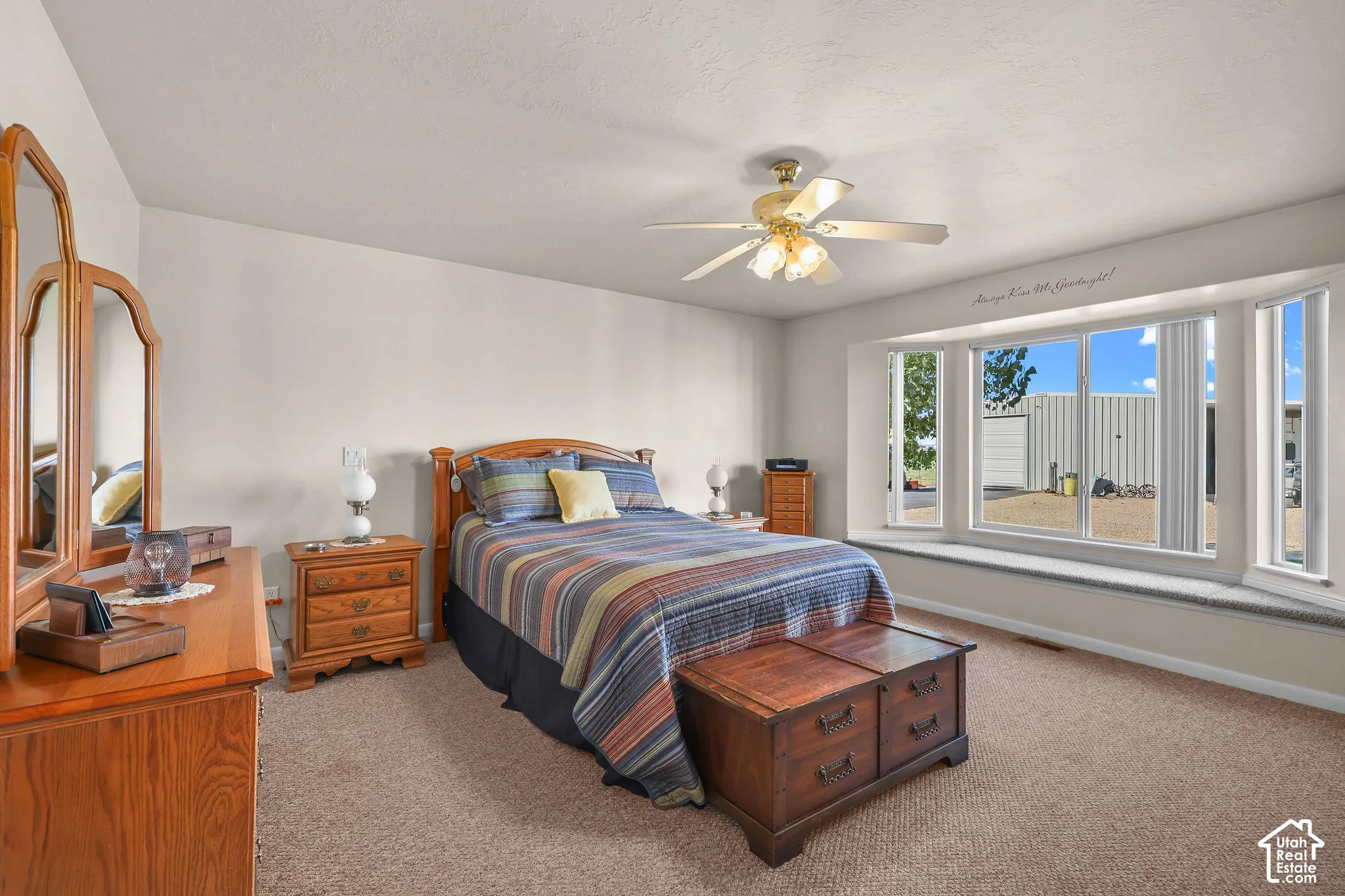 Spacious room featuring a large bay window, integrated built-in window seat, neutral carpeting, and a ceiling fan with integrated lighting