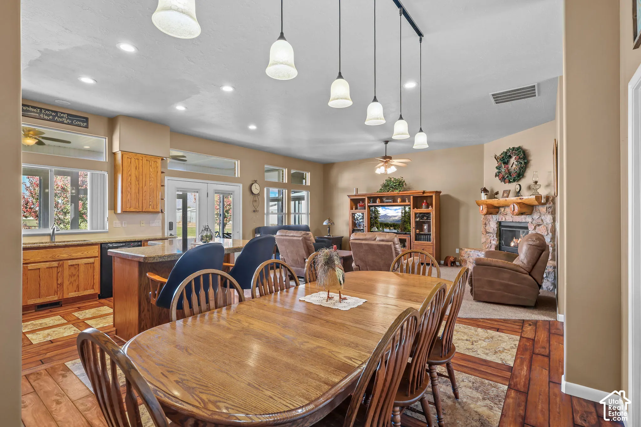 Open-concept interior featuring wood-look flooring, stone fireplace with log mantel, recessed lighting, and kitchen island with pendant fixtures