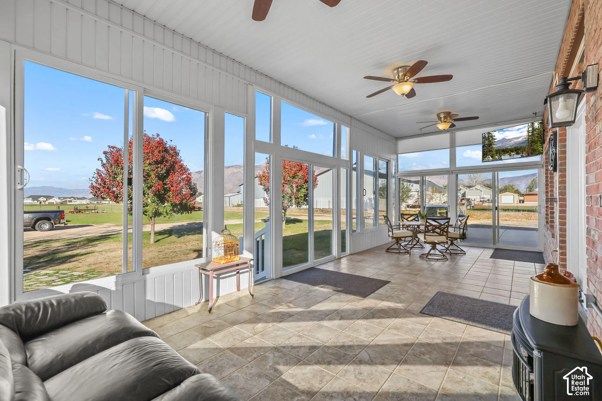Enclosed sunroom featuring tile flooring, beadboard paneling, expansive floor-to-ceiling windows, and dual ceiling fans