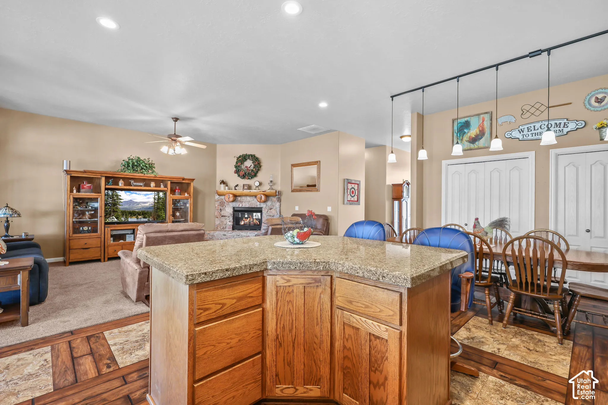 Kitchen island featuring wood cabinetry and stone-finish countertop, stone-accented corner fireplace, wooden media center, and multi-pendant island lighting