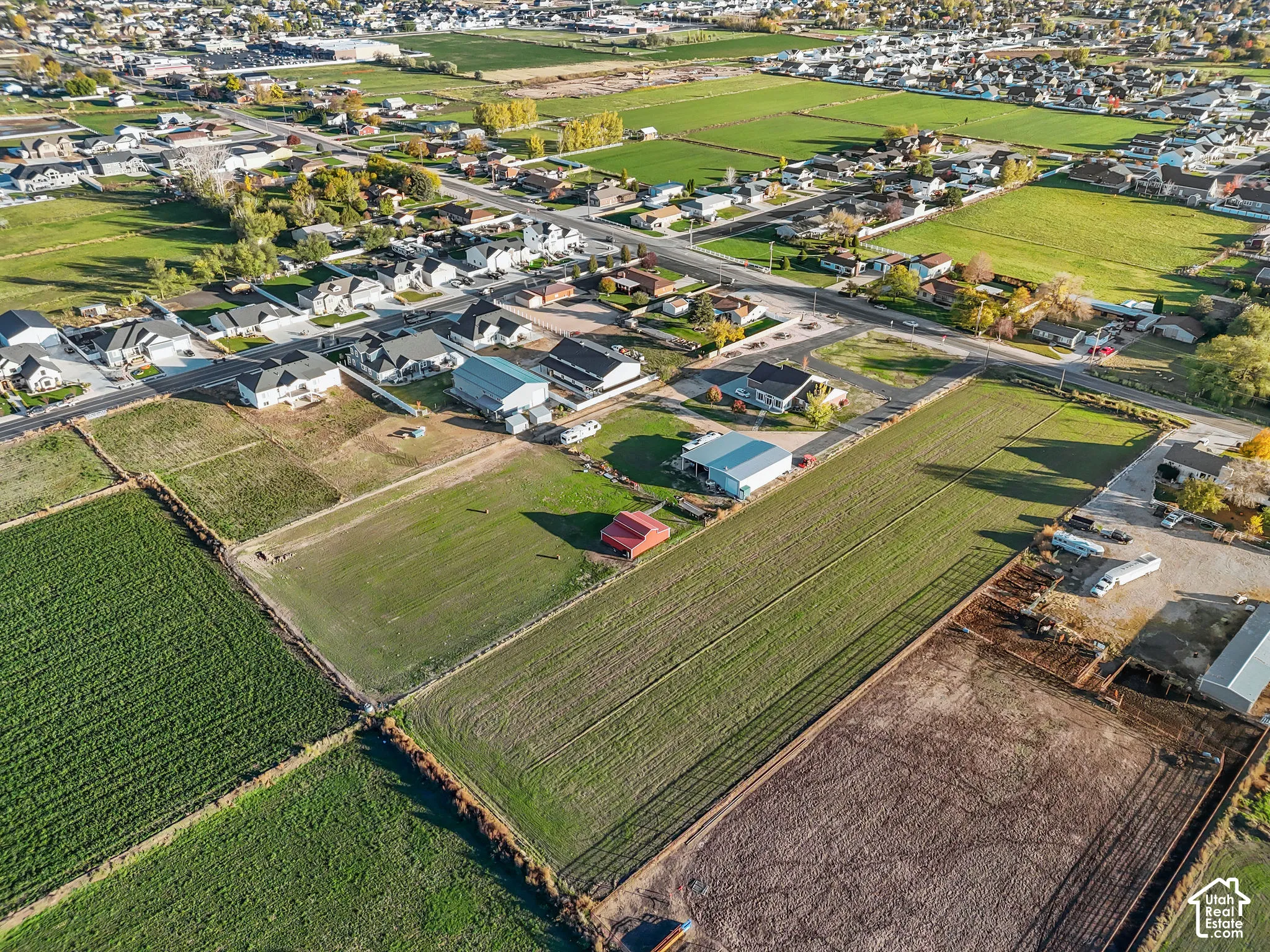 Aerial perspective of expansive acreage featuring open fields, a metal-roofed structure, and an outbuilding