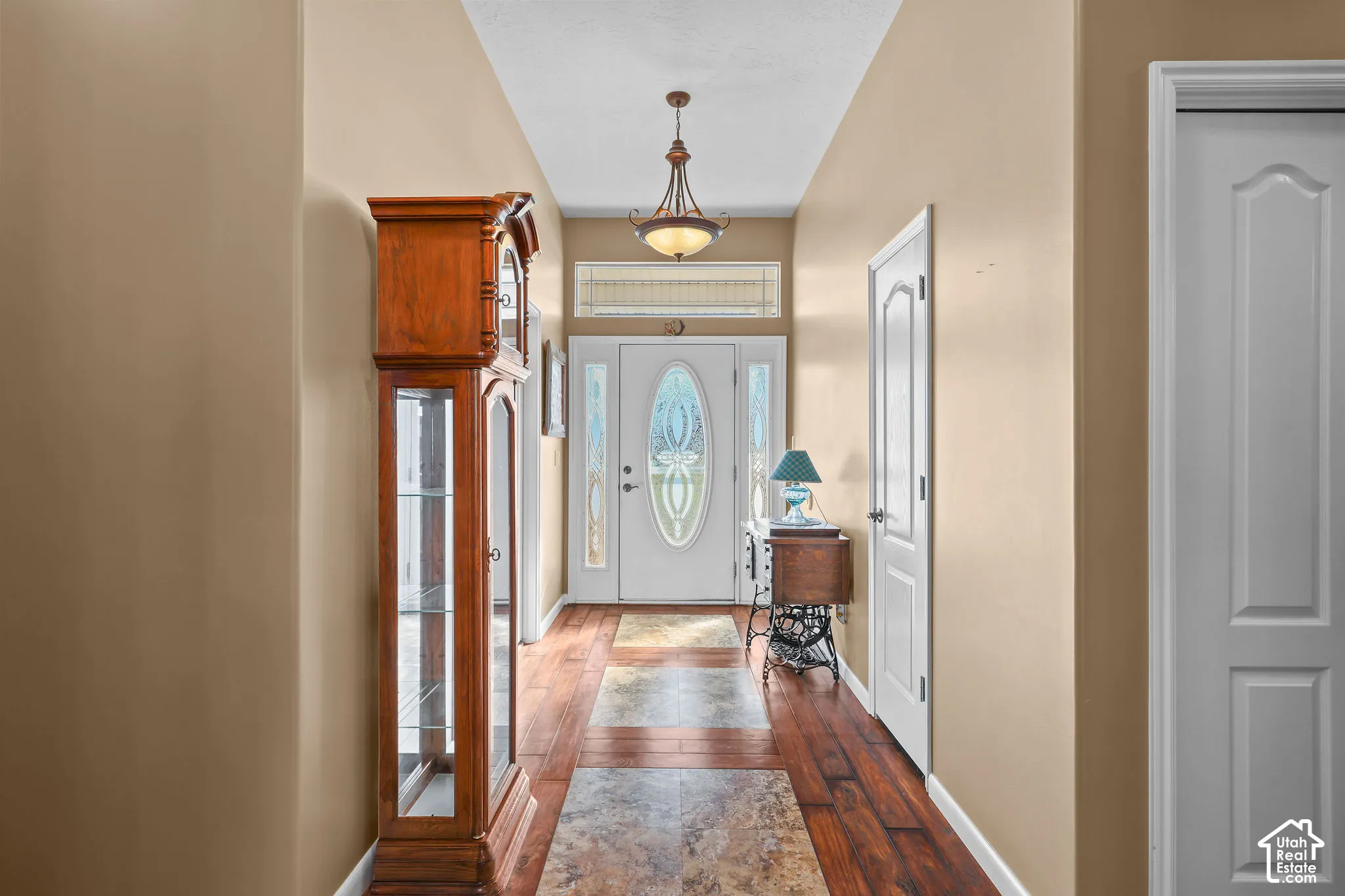 Entryway featuring an oval-glass paneled front door, transom window, dual sidelights, wood-finish flooring with tile inlays, and a multi-arm pendant light fixture