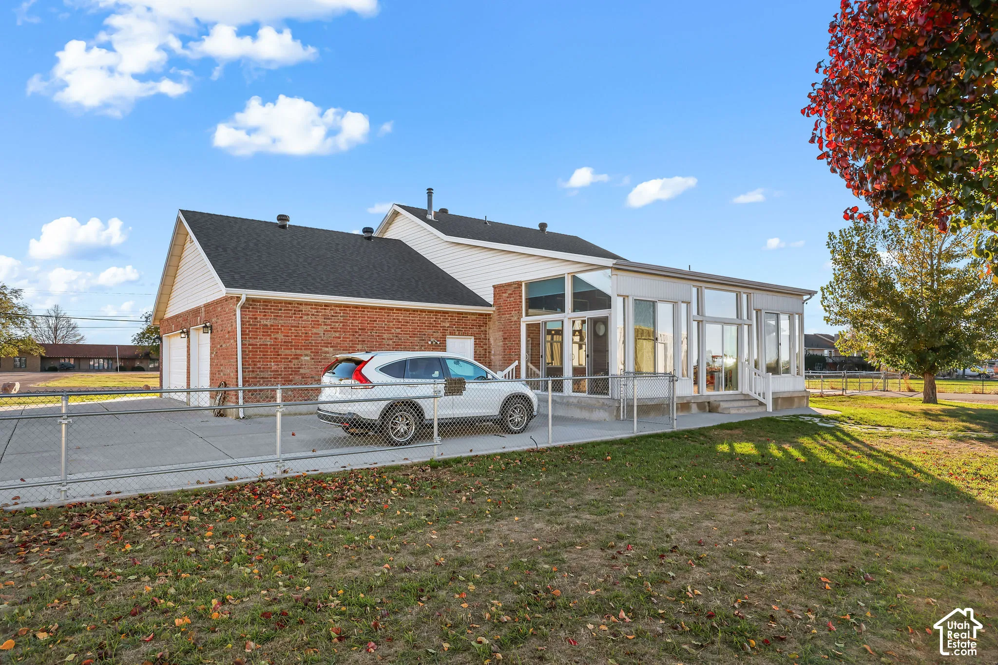 Exterior featuring brick and horizontal siding, an attached two-car garage, and a glass-enclosed sunroom with an expansive concrete patio