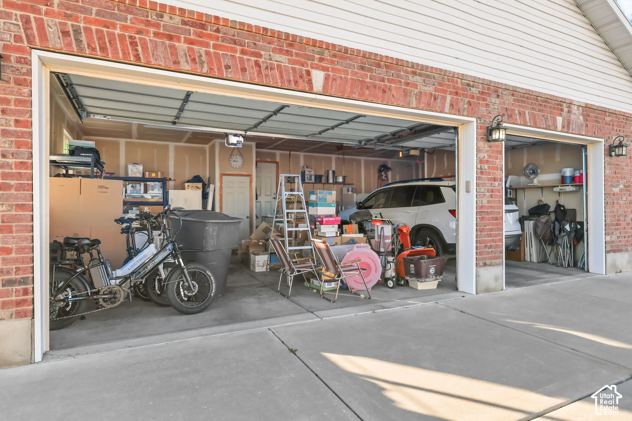 Attached three-car garage featuring red brick veneer exterior, white horizontal siding, concrete flooring, and metal carriage-style wall sconces