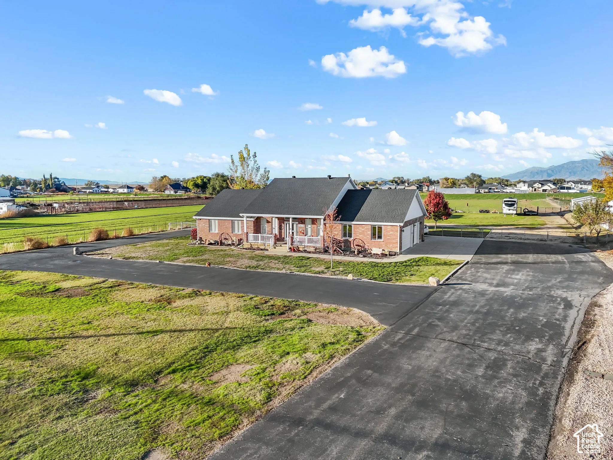 Single-story brick exterior residence featuring a covered front porch, asphalt-shingled roof, attached garage, and an expansive paved driveway situated on a large lot