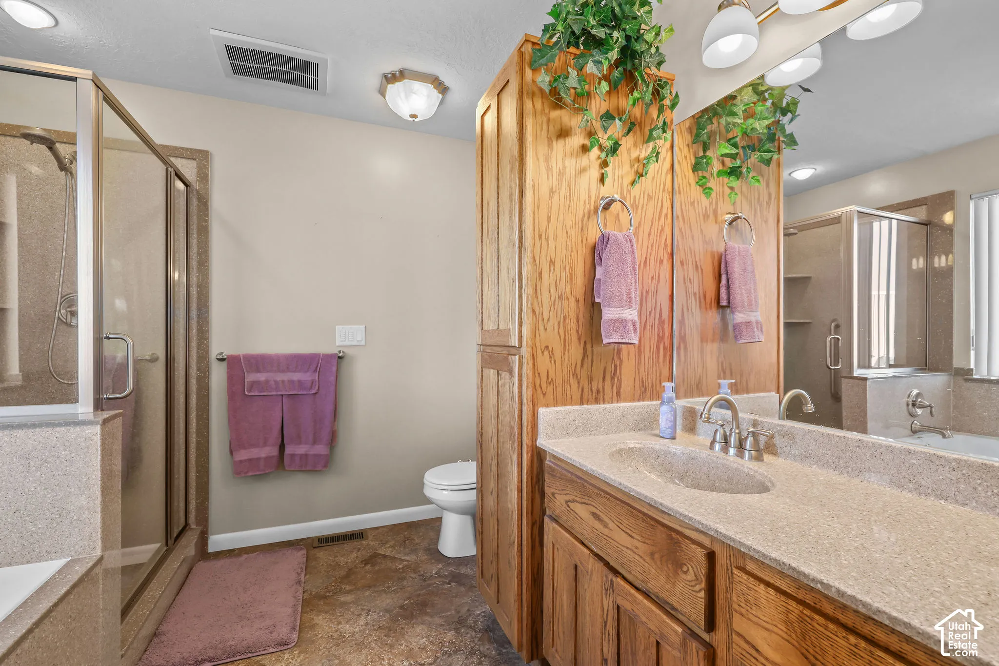 Bathroom featuring a walk-in shower with glass enclosure, built-in floor-to-ceiling wood cabinetry, solid-surface vanity countertop with integrated sink, and large wall-mounted mirror