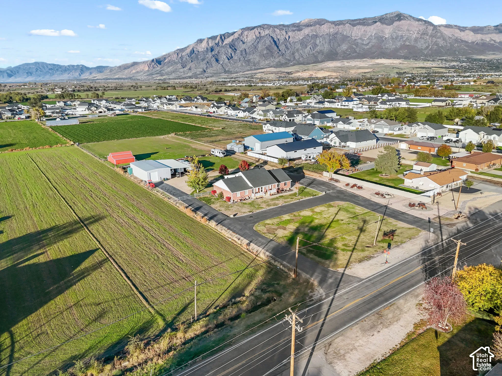 Aerial view featuring a multi-acre parcel with mountain backdrops, a brick-facade residence, detached outbuildings, and expansive open fields