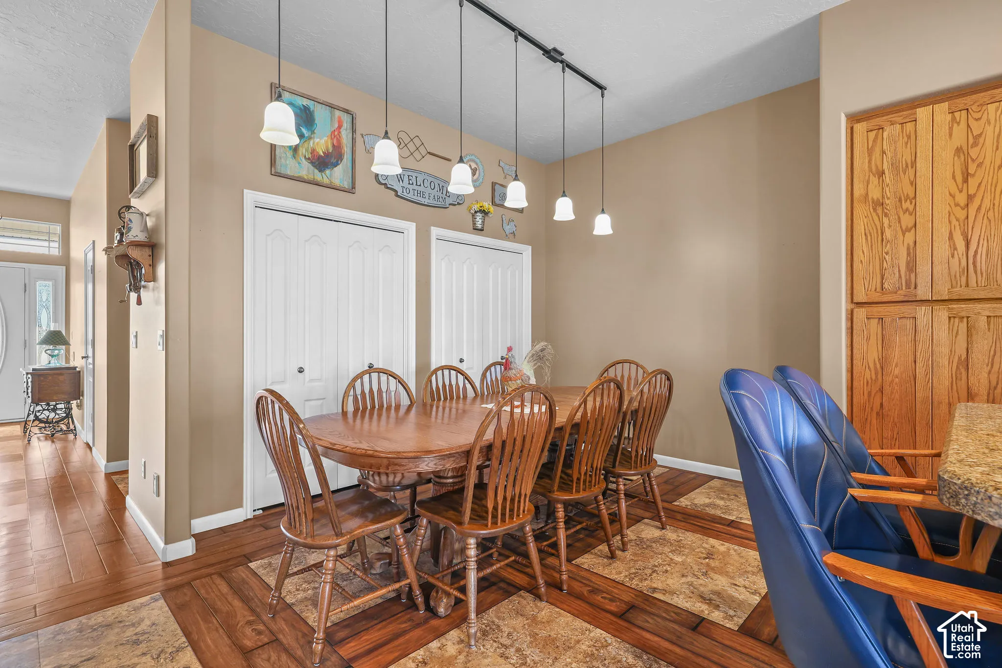 Dining area featuring wood-look flooring with inset stone-tile detailing, a multi-pendant track lighting fixture, tall wood-panel cabinetry, and two sets of white bifold closet doors