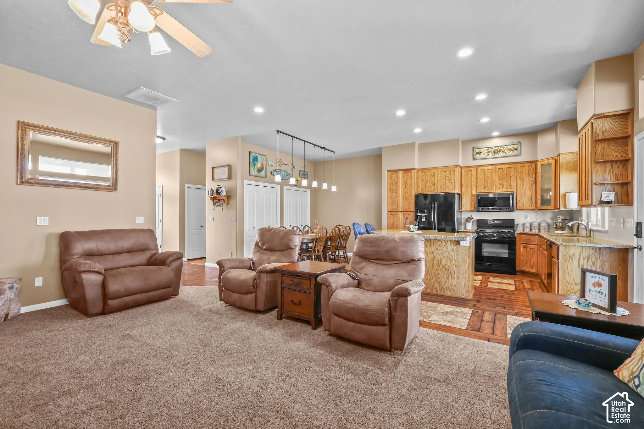 Open-concept interior featuring wood cabinetry, recessed lighting, a multi-light pendant fixture, wood-look flooring, and a ceiling fan