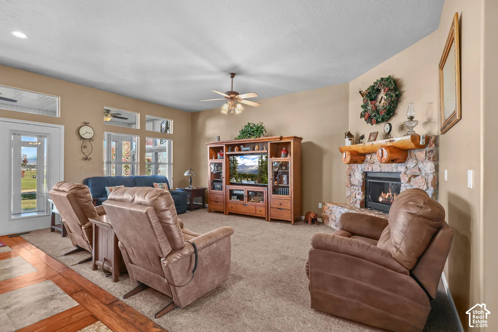 Living area featuring a stone fireplace with a natural log mantle, wooden cabinetry, neutral carpeting, and multi-paned windows