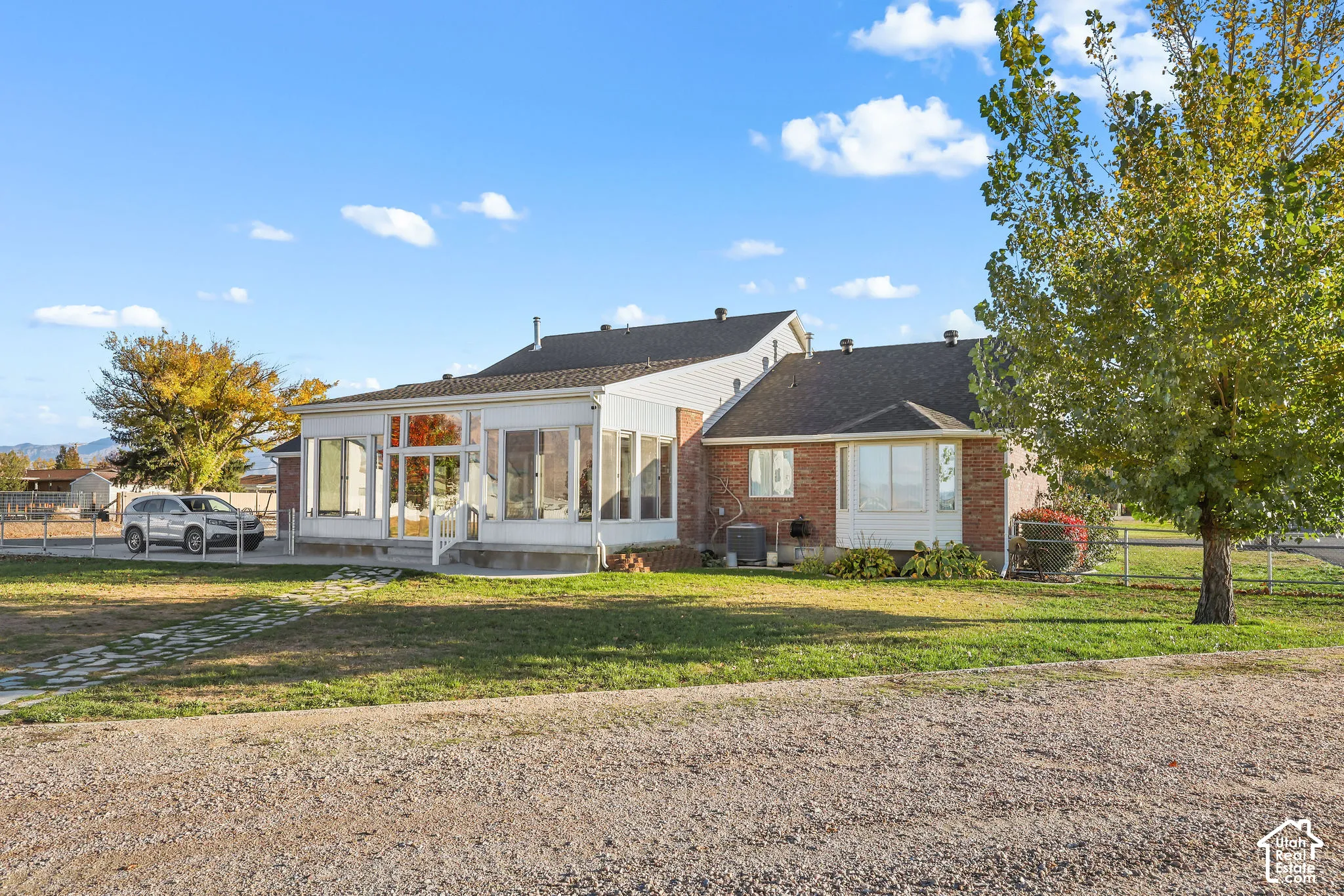 Brick and siding exterior featuring an enclosed sunroom, bay window, stone walkway, and perimeter fencing