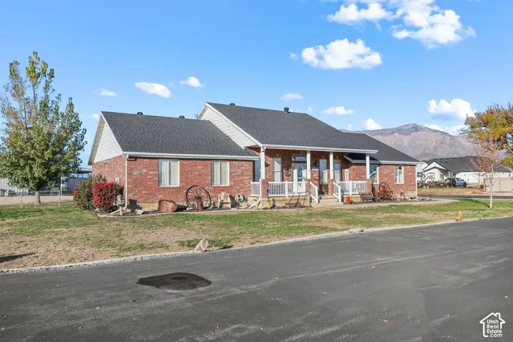 Red brick exterior featuring horizontal siding, asphalt shingle roofing, and a covered front porch with white railings against a mountain backdrop