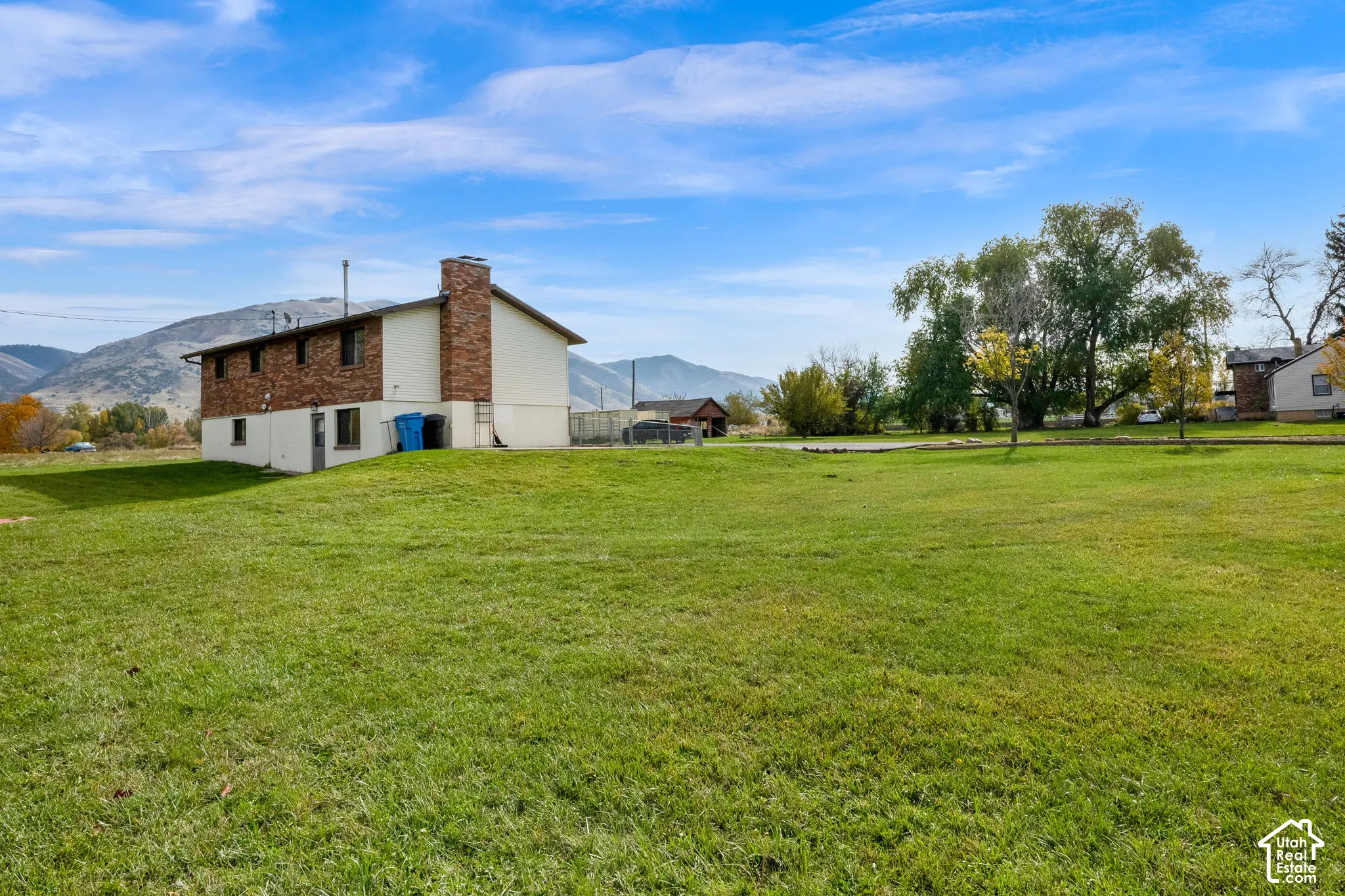 Expansive lot featuring a manicured lawn, brick chimney, and prominent mountain backdrop