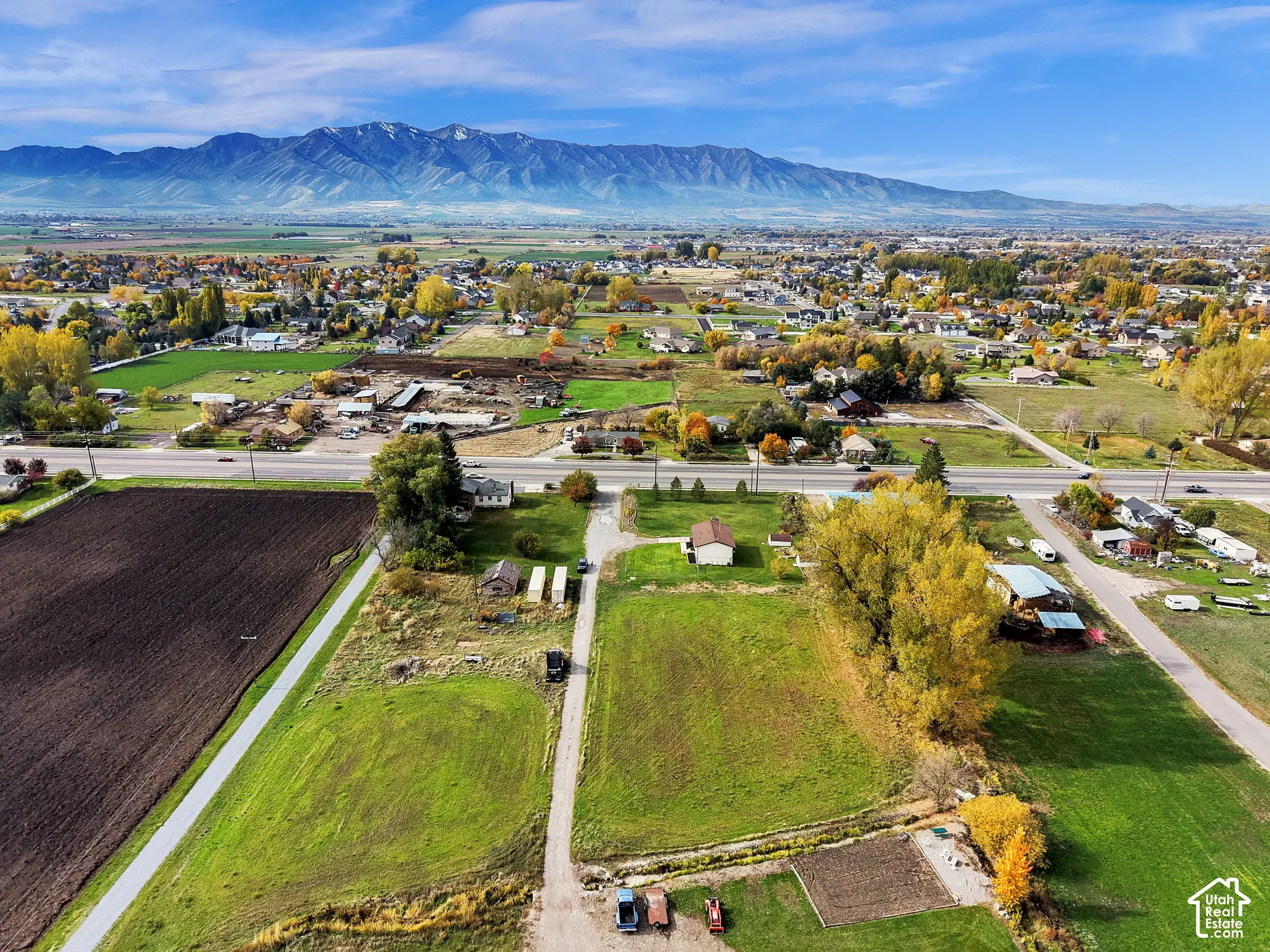 Aerial perspective of expansive acreage featuring open grass fields, mature trees, and a mountainous backdrop