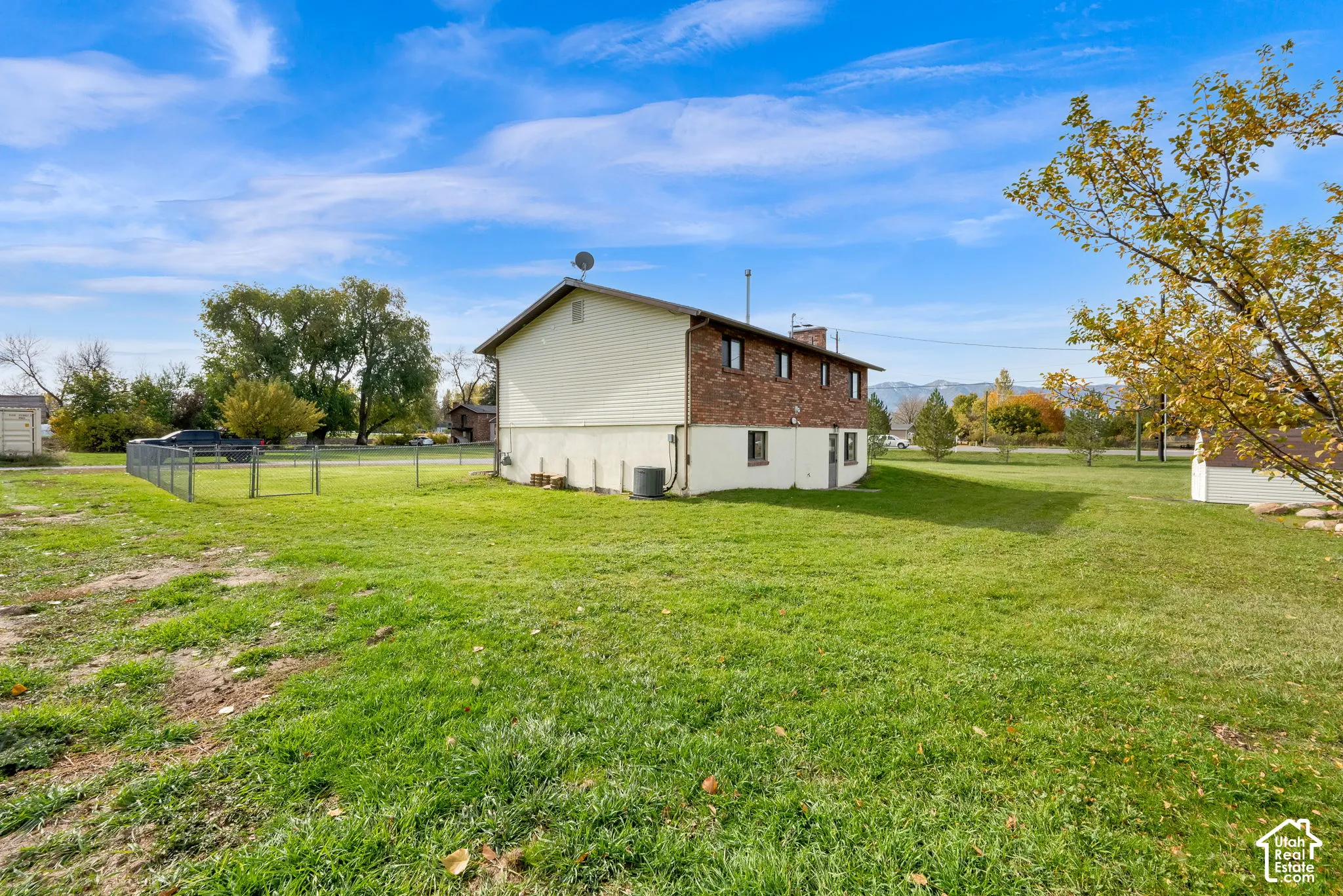 Expansive lot featuring brick and horizontal siding exterior, chain-link fencing, and mature trees