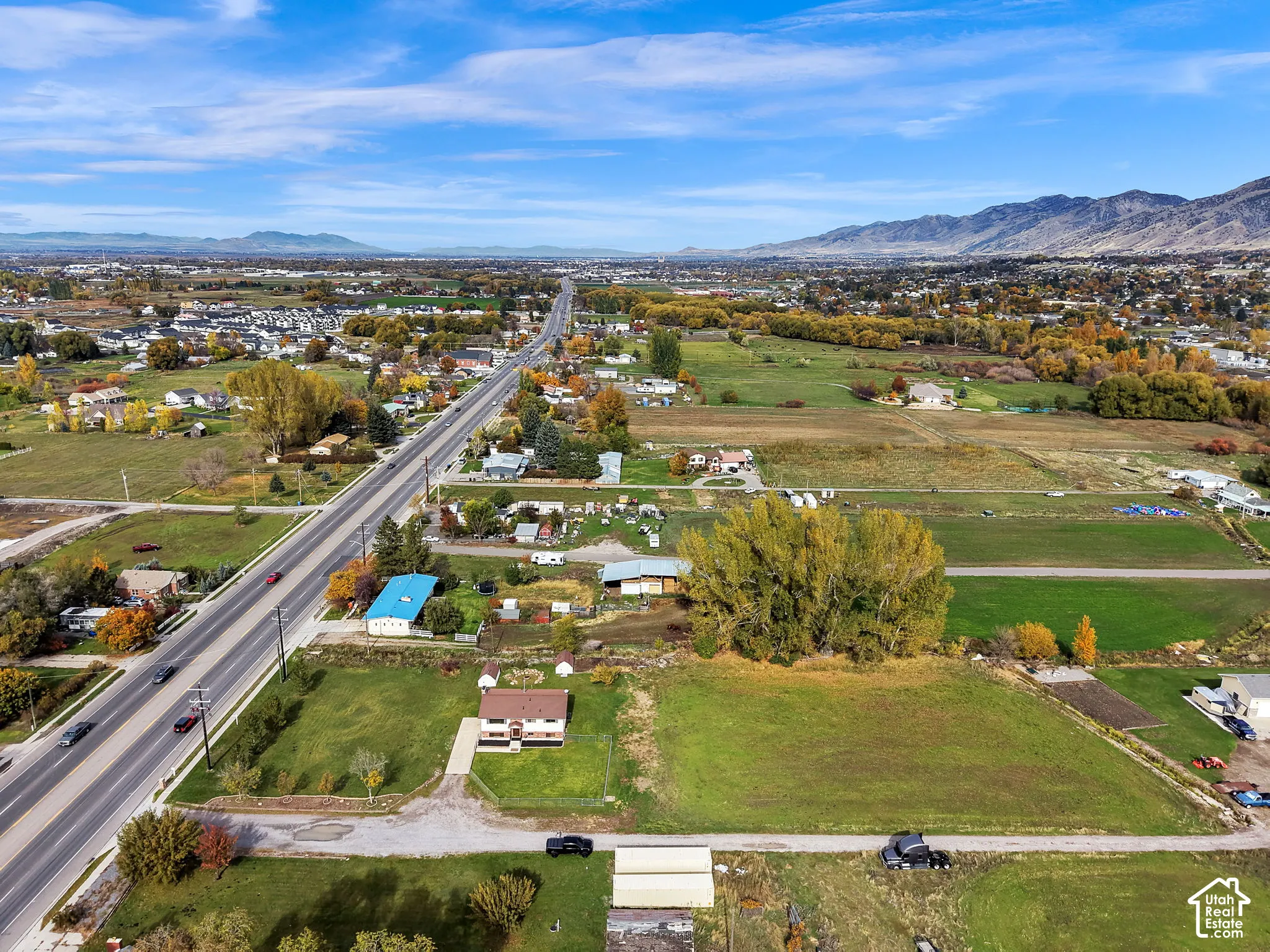 Aerial perspective featuring expansive acreage, mature tree stands, mountain range backdrop, and paved road access