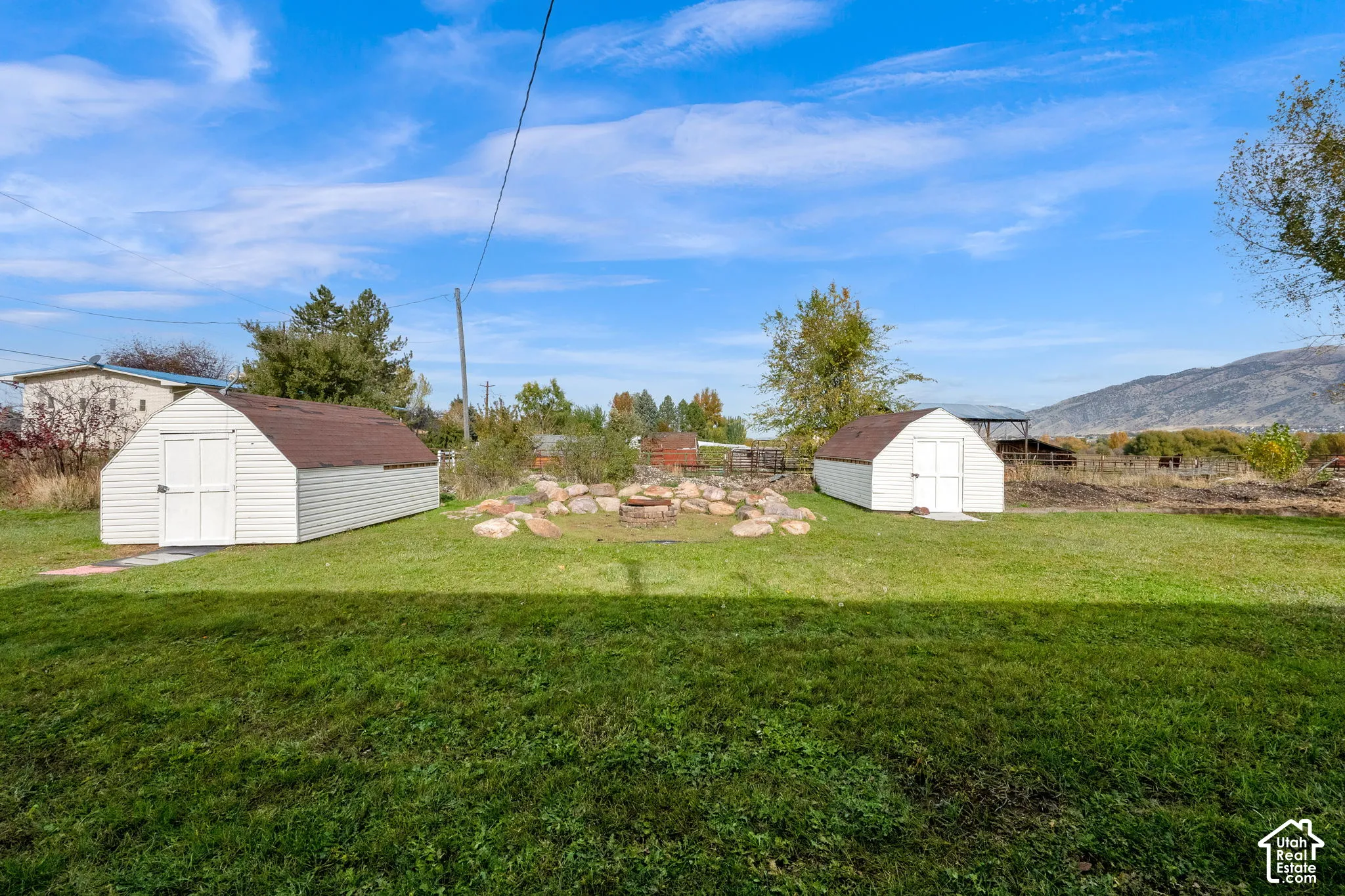 Expansive grounds featuring two detached storage structures, a stone-bordered fire pit, and mountain scenery