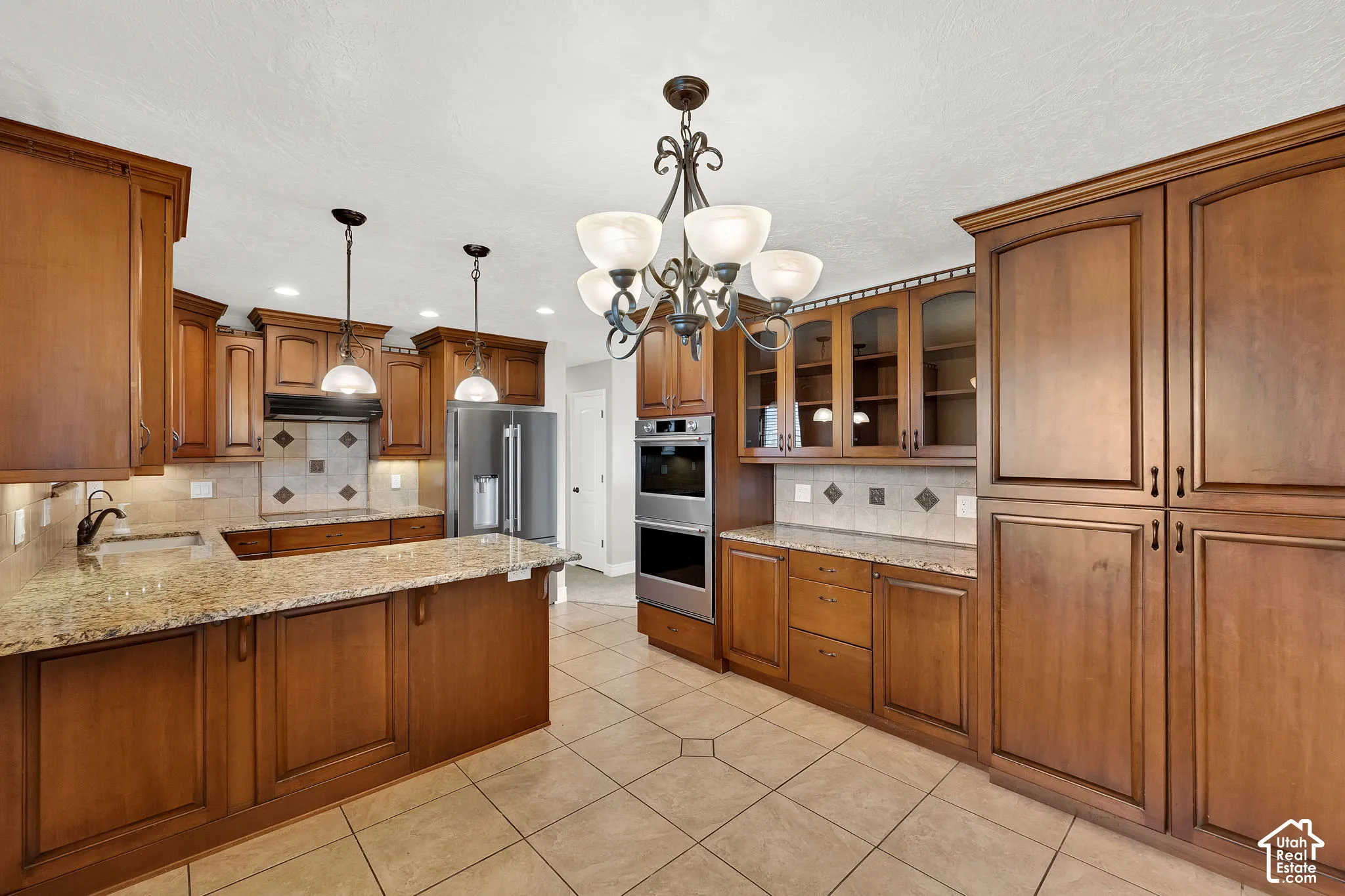 Kitchen featuring medium-toned wood cabinetry, stone countertops, double wall ovens, glass-front upper cabinets, and tile flooring