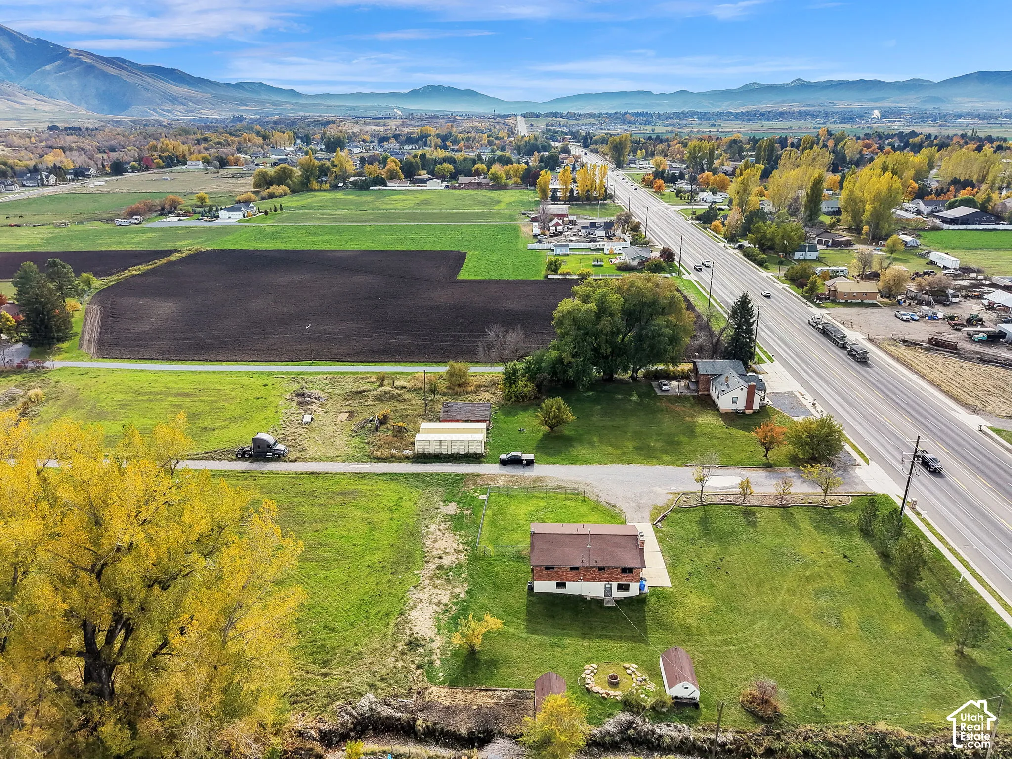 Aerial perspective of expansive acreage featuring mature trees, a dedicated fire pit area with stone hardscaping, and a mountainous backdrop